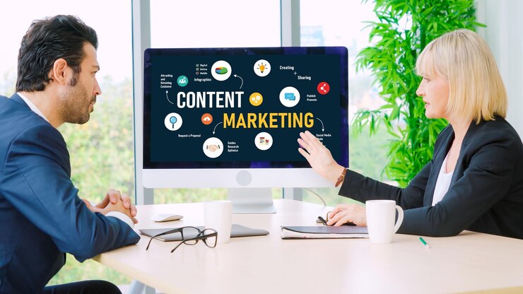 Two marketing professionals discussing content strategy in an office setting with a computer screen displaying a content marketing diagram.
