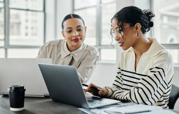 Two marketing professionals collaborating at a desk with laptops, discussing social media strategy and content planning in a bright modern office.